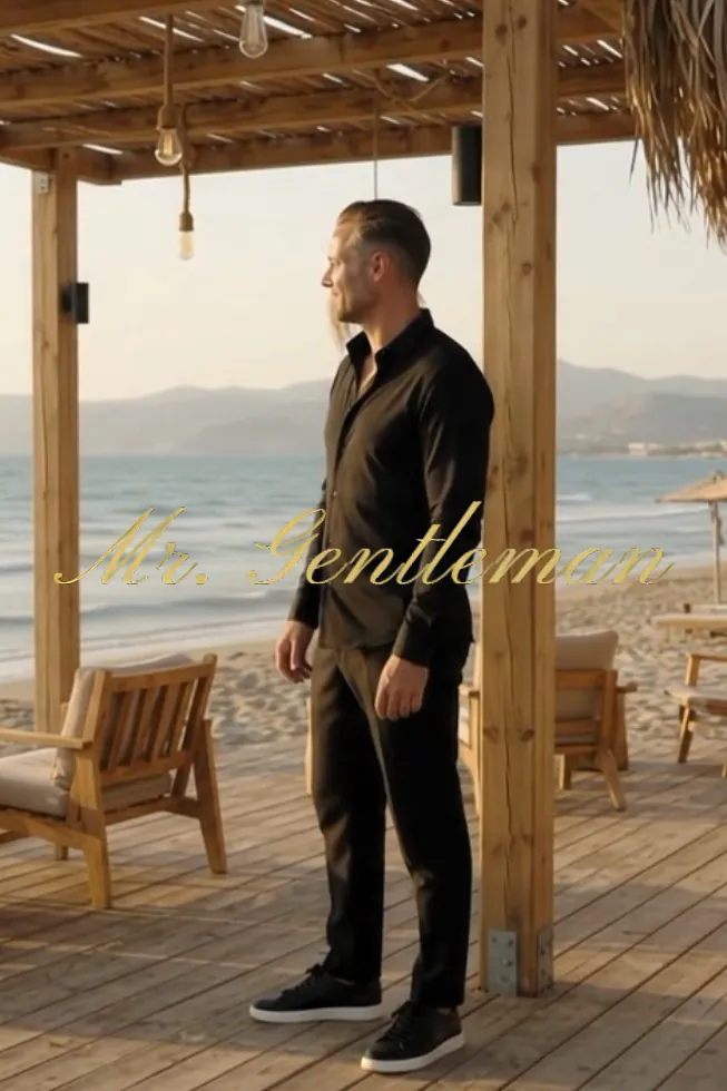 Mr. Gentleman in black, standing under a beach pergola by the sea in Crete