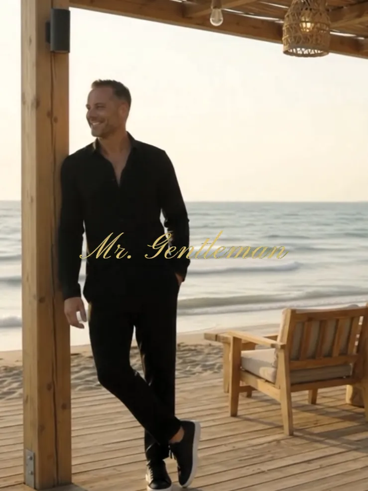 Mr. Gentleman in black, leaning on a post of a wooden beach deck in Bali, Crete