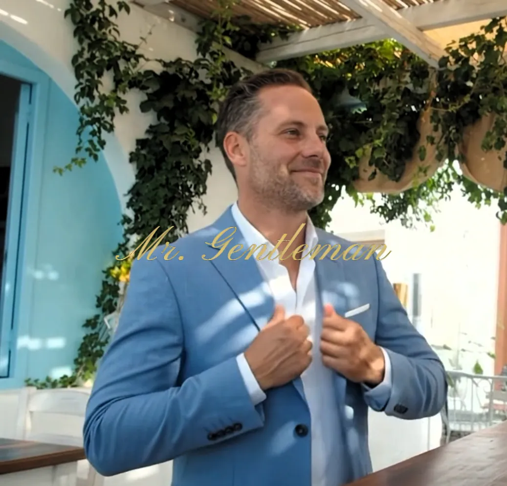 Laughing Mr. Gentleman in a light blue blazer on a vine-covered terrace in Crete
