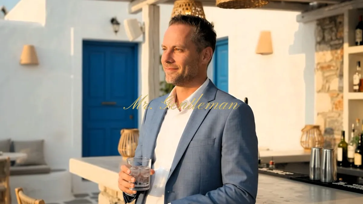 Mr. Gentleman in a blazer with a drink by a blue Cretan door in Bali, Crete
